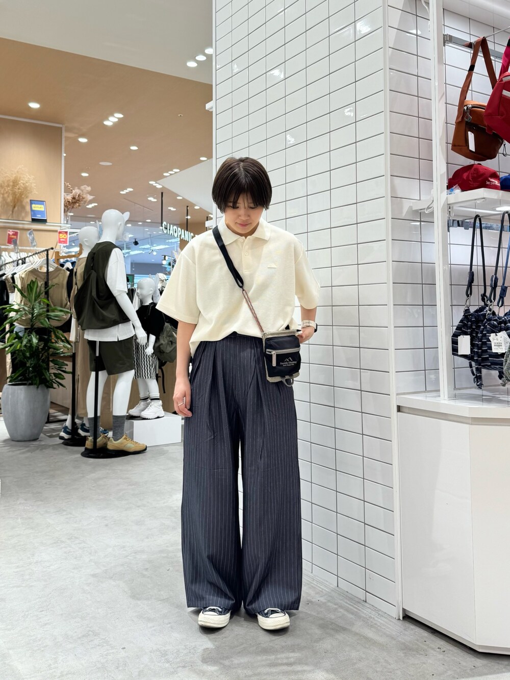 グレー系のスラックス、ホワイト系のポロシャツ、ベージュ系のショルダーバッグを着用したレディースの夏コーディネートの3枚目の写真