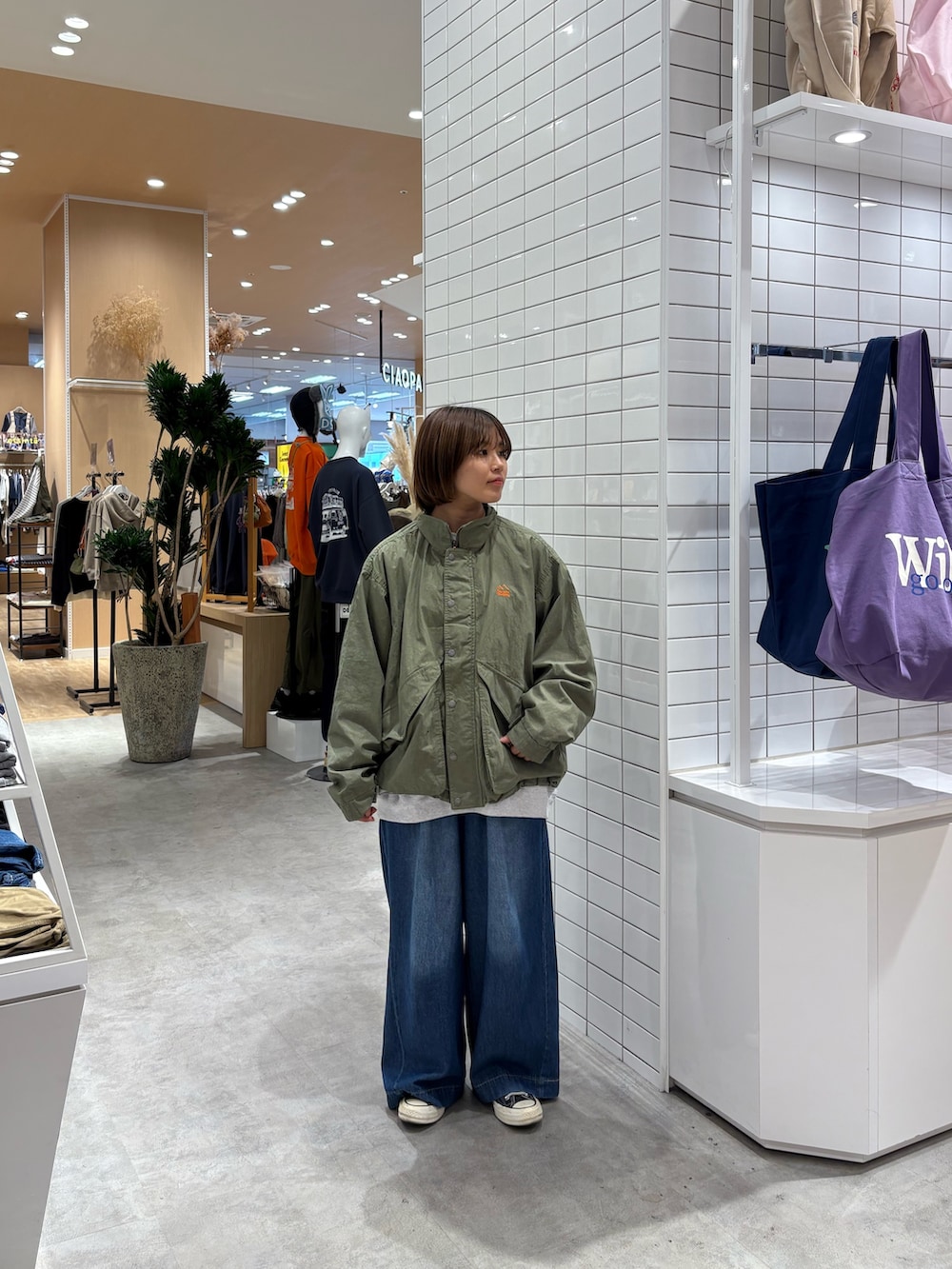 グレー系のスウェット、ブルー系のデニムパンツ、グリーン系のナイロンジャケットを着用したレディースの秋コーディネートの3枚目の写真