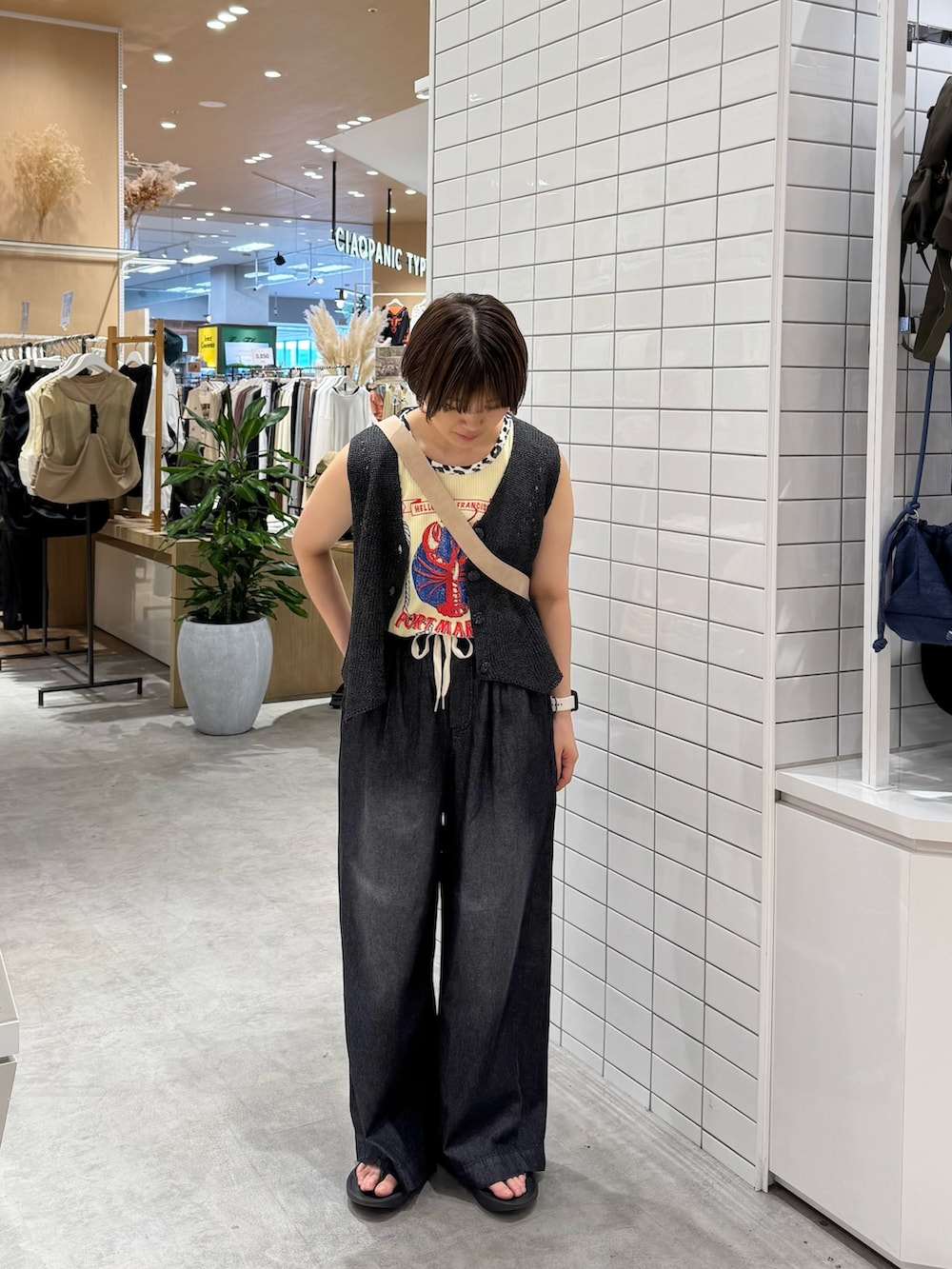 ホワイト系のショルダーバッグ、ブラック系のデニムパンツ、グレー系のベストを着用したレディースの夏コーディネートの2枚目の写真