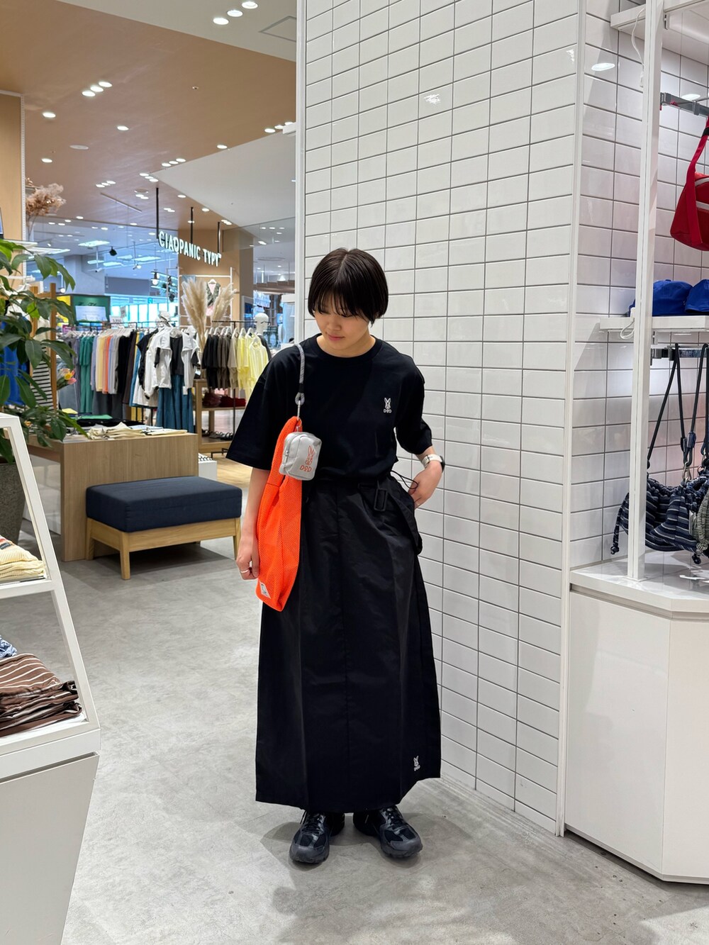 ブラック系のTシャツ/カットソー、ブラック系のスカート、オレンジ系のトートバッグを着用したレディースの春コーディネートの2枚目の写真