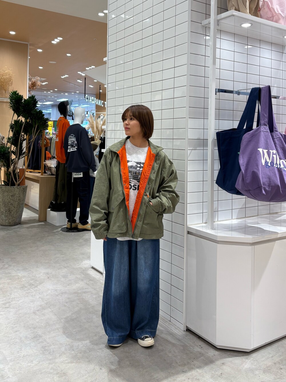 グレー系のスウェット、ブルー系のデニムパンツ、グリーン系のナイロンジャケットを着用したレディースの秋コーディネートの2枚目の写真