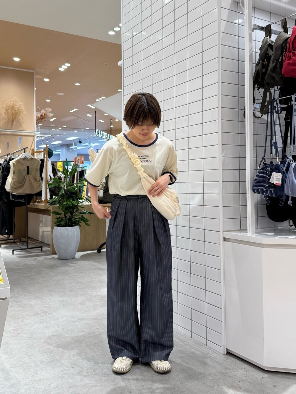 グレー系のスラックス、ホワイト系のトートバッグ、ホワイト系のTシャツ/カットソーを着用したレディースの夏コーディネートの2枚目の写真