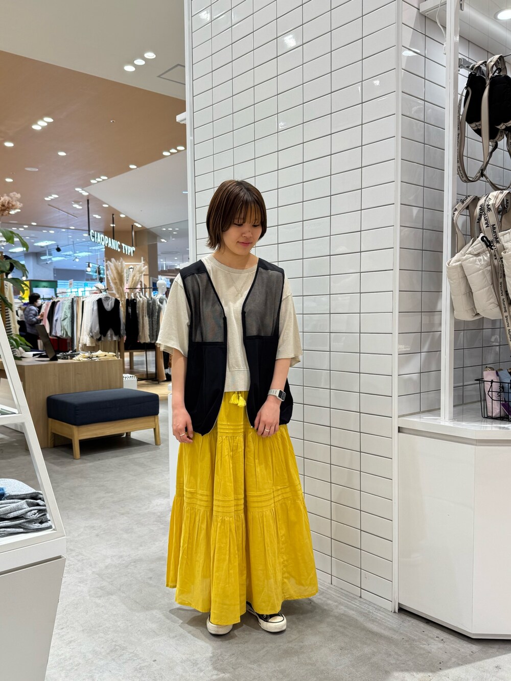グレー系のTシャツ/カットソー、ブラック系のベスト、イエロー系のスカートを着用したレディースの春コーディネートの3枚目の写真