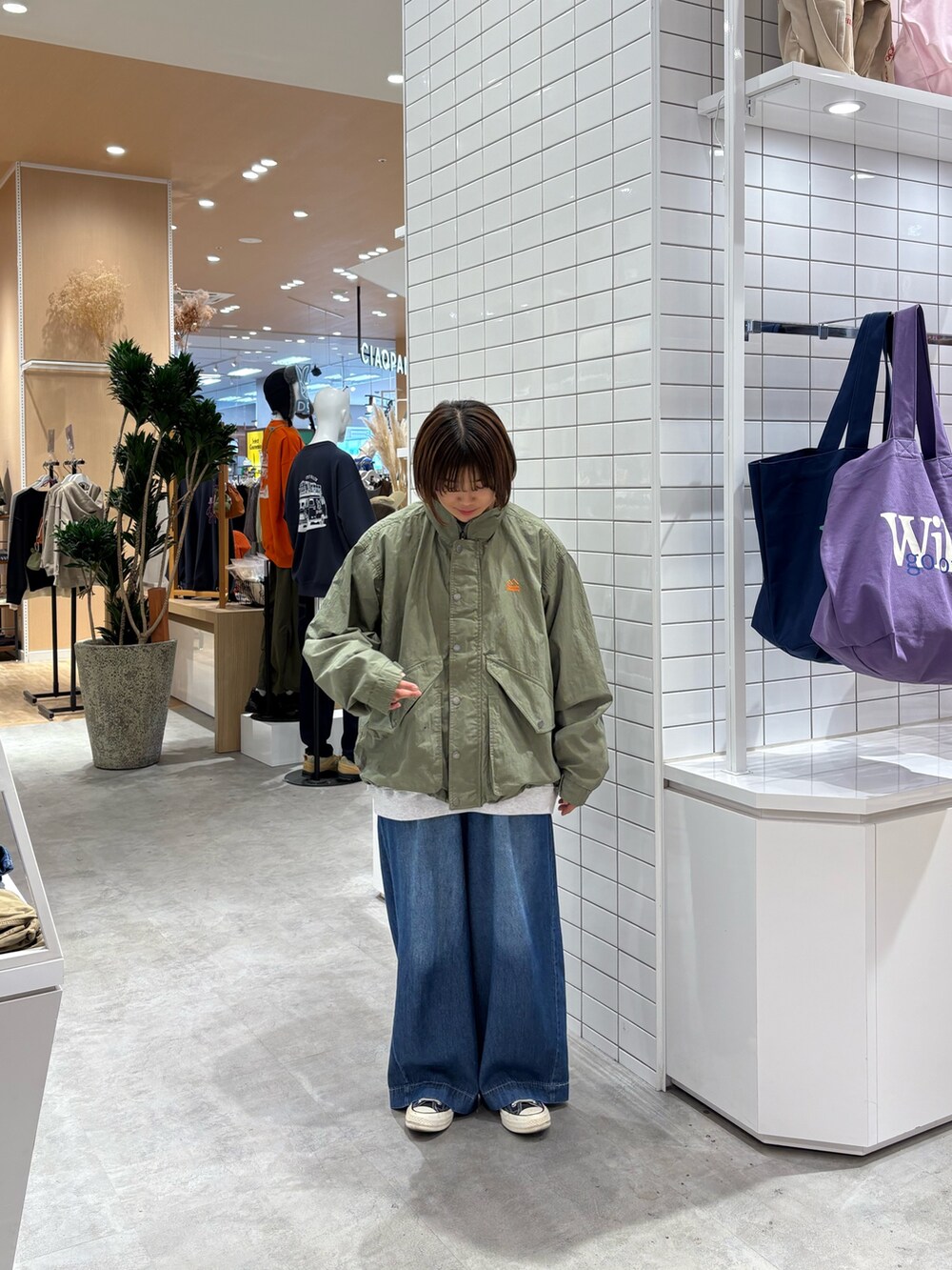 グレー系のスウェット、ブルー系のデニムパンツ、グリーン系のナイロンジャケットを着用したレディースの秋コーディネートの4枚目の写真