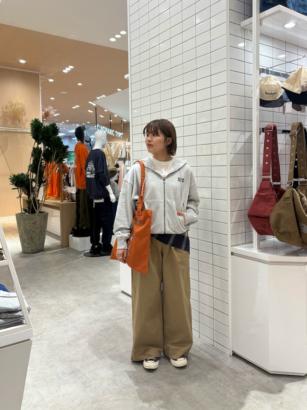 グレー系のパーカー、ベージュ系のデニムパンツ、オレンジ系のトートバッグを着用したレディースの秋コーディネートの3枚目の写真