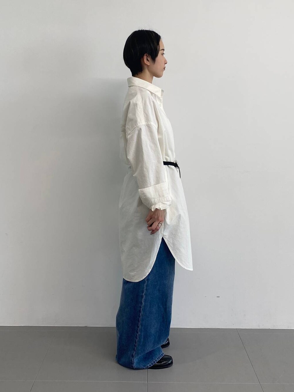 ブルー系のデニムパンツ、ホワイト系のシャツワンピース、ブラック系のベルトを着用したレディースの冬コーディネートの2枚目の写真