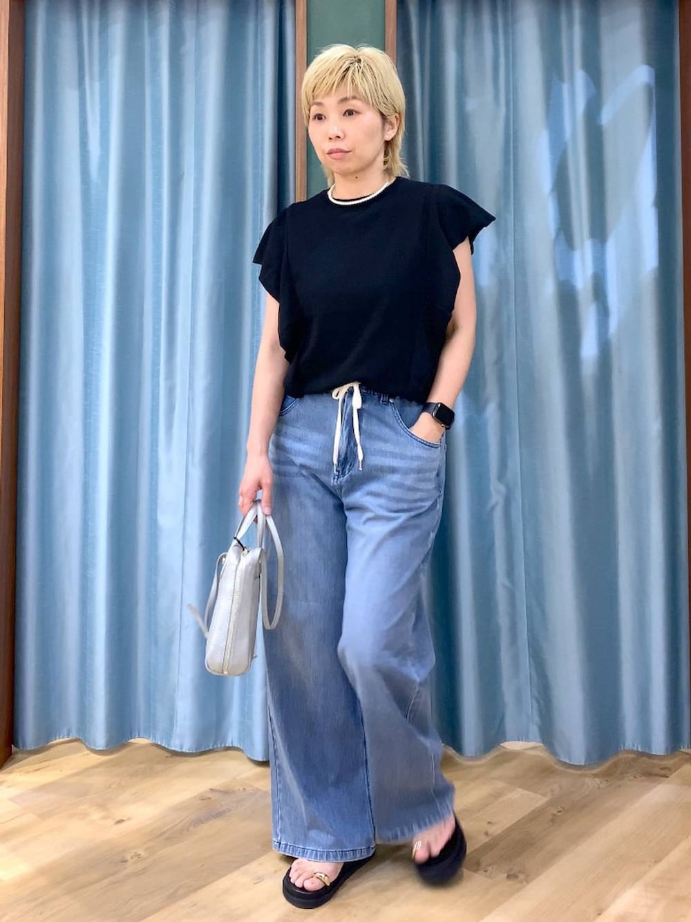 ブルー系のデニムパンツ、シルバー系のショルダーバッグ、ブラック系のニット/セーターを着用したレディースの夏コーディネートの5枚目の写真
