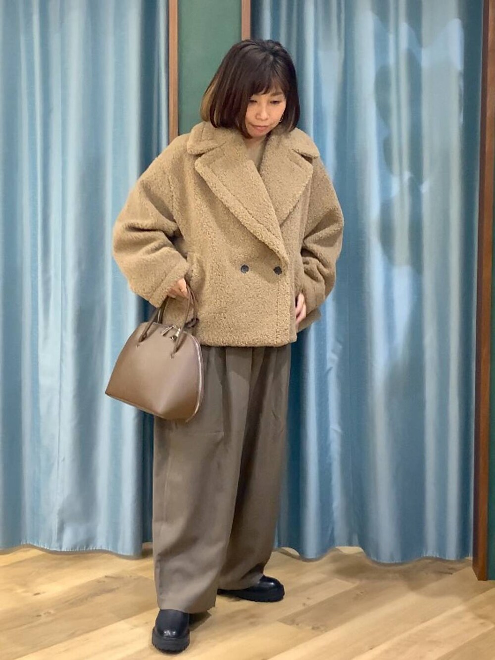 ブラック系のブーツ、ベージュ系のピーコート、ブラウン系のトートバッグを着用したレディースの秋コーディネートの2枚目の写真