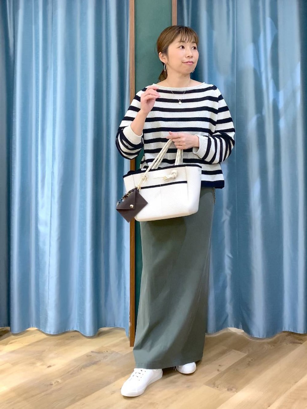 ベージュ系のニット/セーター、グリーン系のスカート、ホワイト系のトートバッグを着用したレディースの春コーディネートの2枚目の写真