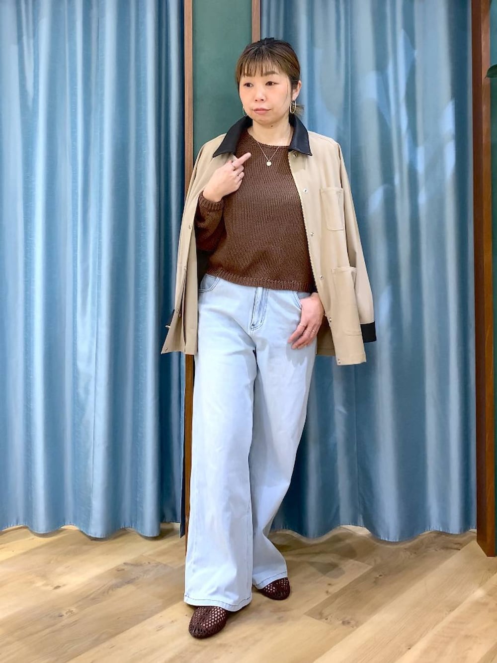 ブルー系のデニムパンツ、ブラウン系のニット/セーター、ベージュ系のカバーオールを着用したレディースの春コーディネートの2枚目の写真