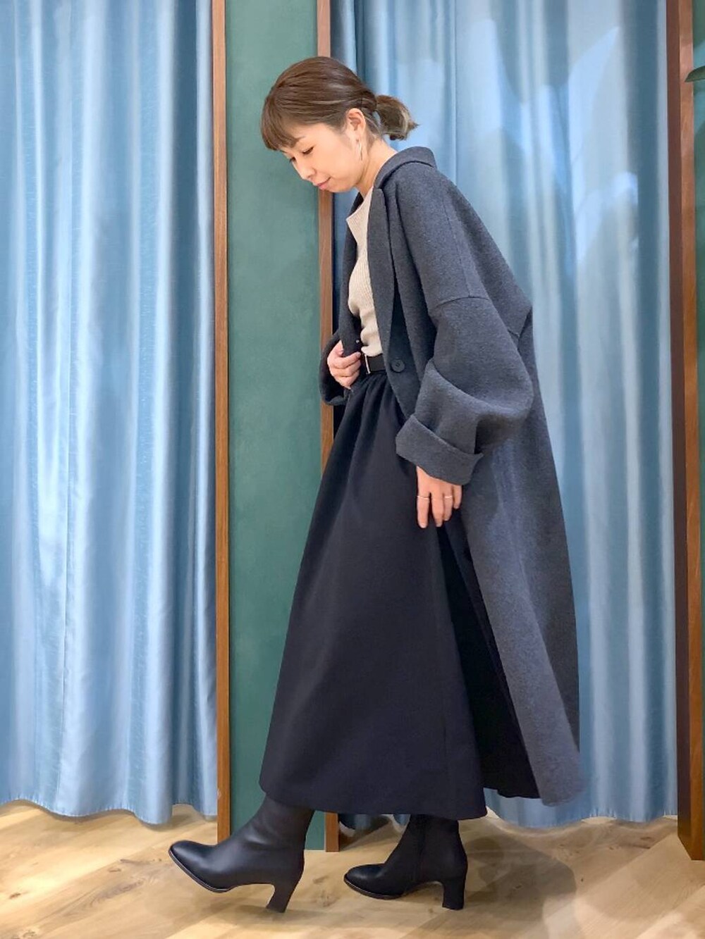 グレー系のチェスターコート、ブラック系のブーツ、ベージュ系のニット/セーターを着用したレディースの冬コーディネートの2枚目の写真