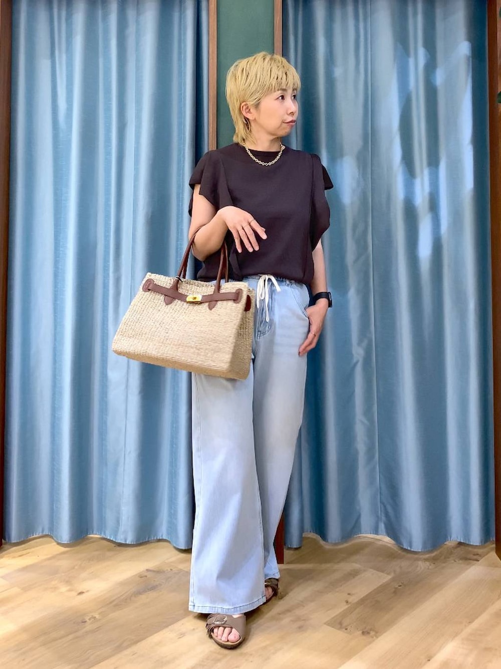ブルー系のデニムパンツ、ブラウン系のニット/セーター、ベージュ系のかごバッグを着用したレディースの夏コーディネートの3枚目の写真