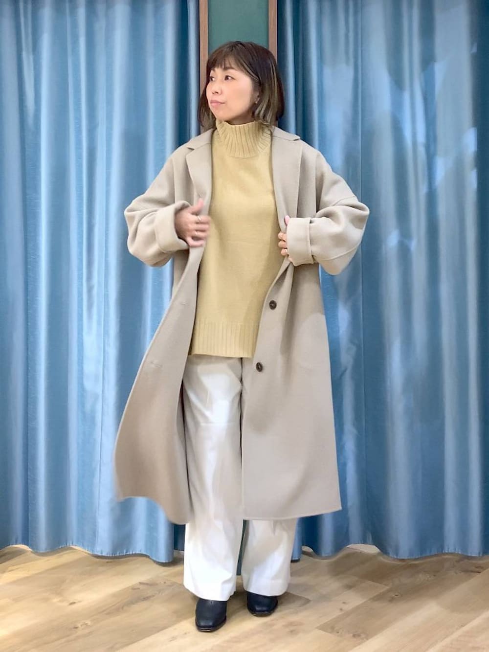 ベージュ系のニット/セーター、ベージュ系のチェスターコート、ブラック系のブーツを着用したレディースの秋コーディネートの2枚目の写真