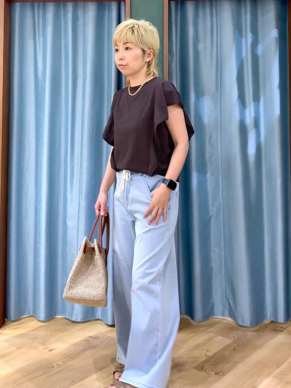ブルー系のデニムパンツ、ブラウン系のニット/セーター、ベージュ系のかごバッグを着用したレディースの夏コーディネートの4枚目の写真