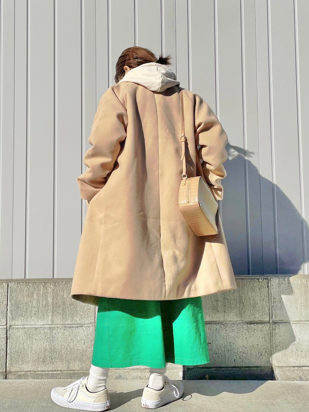 ベージュ系のステンカラーコート、ベージュ系のショルダーバッグ、グリーン系のワンピースを着用したレディースの秋コーディネートの3枚目の写真