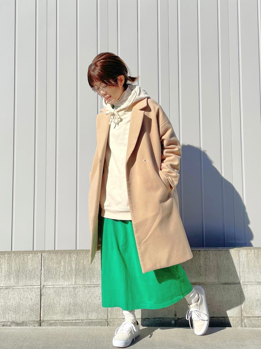 ベージュ系のステンカラーコート、ベージュ系のショルダーバッグ、グリーン系のワンピースを着用したレディースの秋コーディネートの2枚目の写真