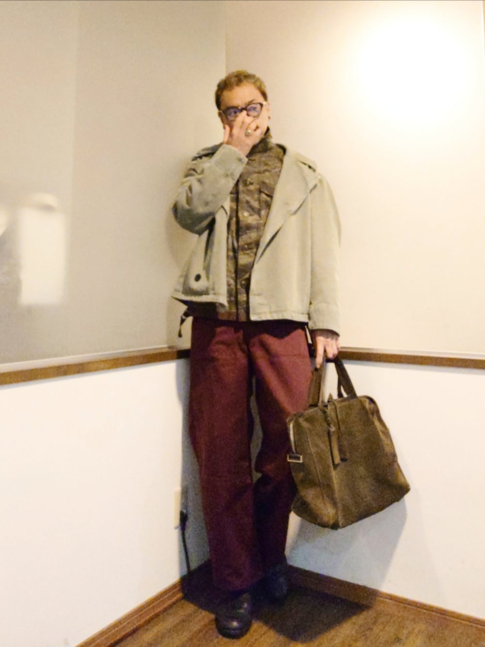 グリーン系のトレンチコート、グリーン系のミリタリージャケット、レッド系のパンツを着用したメンズの秋コーディネートの2枚目の写真