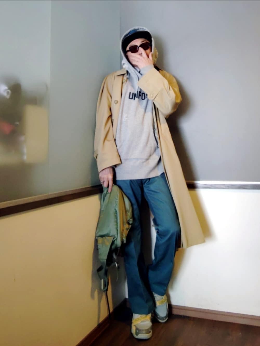 ベージュ系のトレンチコート、グリーン系のボディバッグ/ウエストポーチ、グリーン系のチノパンツを着用したメンズの春コーディネートの2枚目の写真