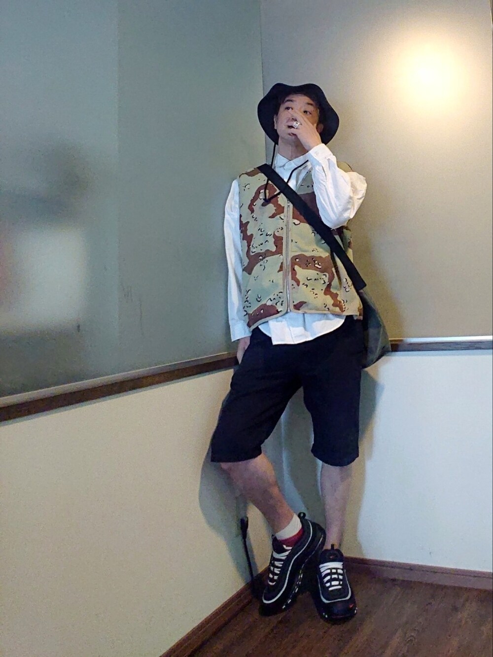 ブラウン系のベスト、グリーン系のショルダーバッグ、ブラック系のチノパンツを着用したメンズの春コーディネートの2枚目の写真