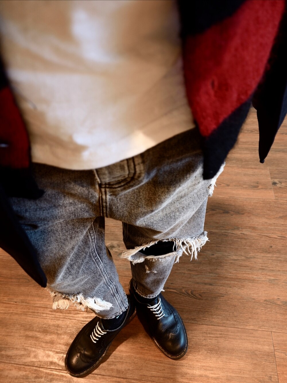 ブラック系のチェスターコート、レッド系のカーディガン/ボレロ、グレー系のデニムパンツを着用したメンズの秋コーディネートの2枚目の写真