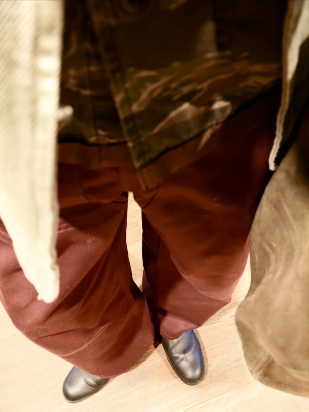 グリーン系のトレンチコート、グリーン系のミリタリージャケット、レッド系のパンツを着用したメンズの秋コーディネートの3枚目の写真