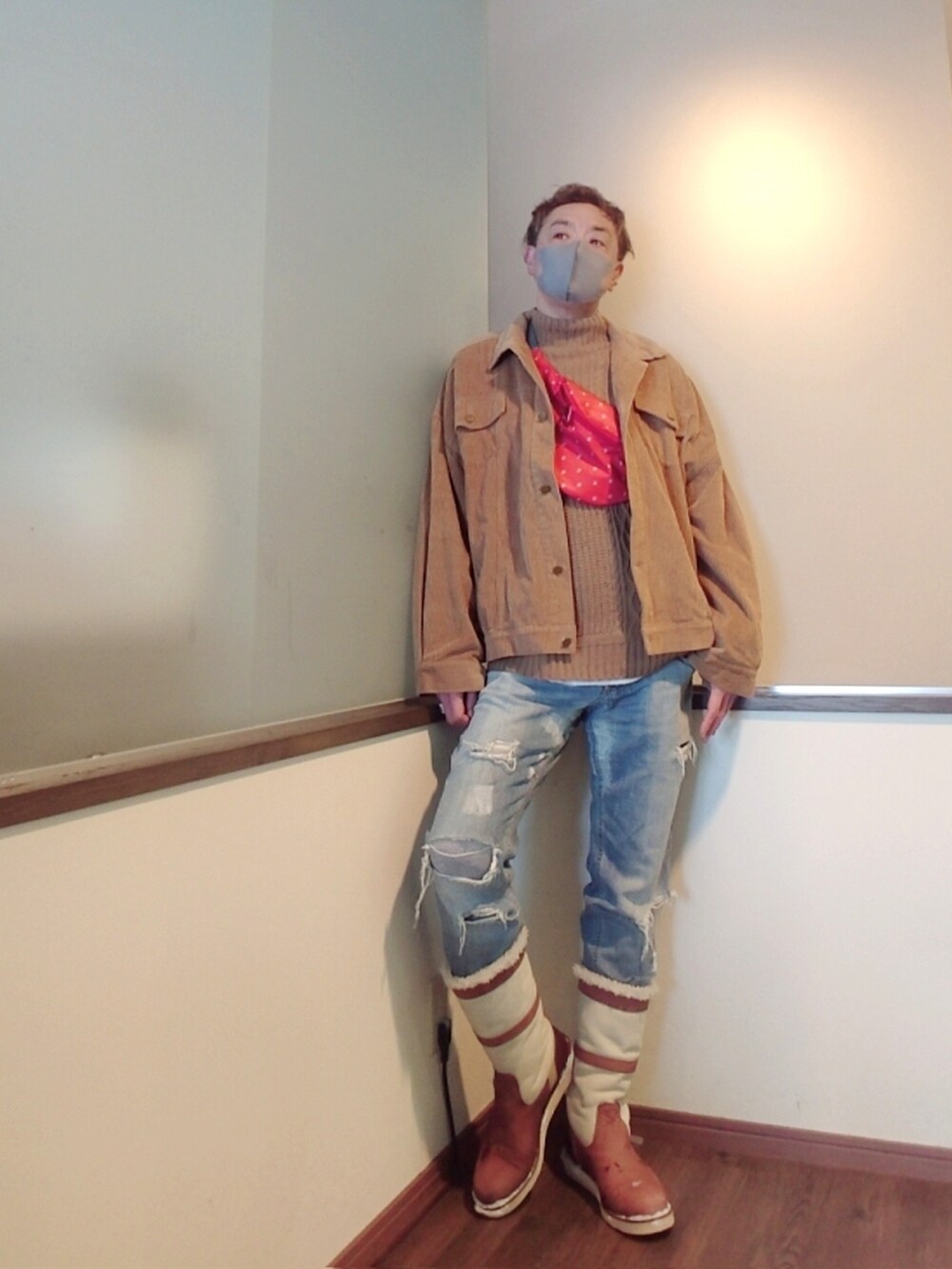 レッド系のショルダーバッグ、ベージュ系のニット/セーター、ブルー系のデニムパンツを着用したメンズの冬コーディネートの2枚目の写真