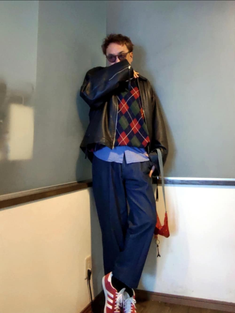 ブルー系のニット/セーター、ブラック系のブルゾン、レッド系のショルダーバッグを着用したメンズの春コーディネートの2枚目の写真