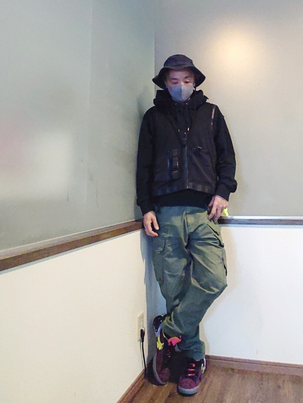 ブラック系のパーカー、ブラック系のベスト、グリーン系のカーゴパンツを着用したメンズの夏コーディネートの2枚目の写真