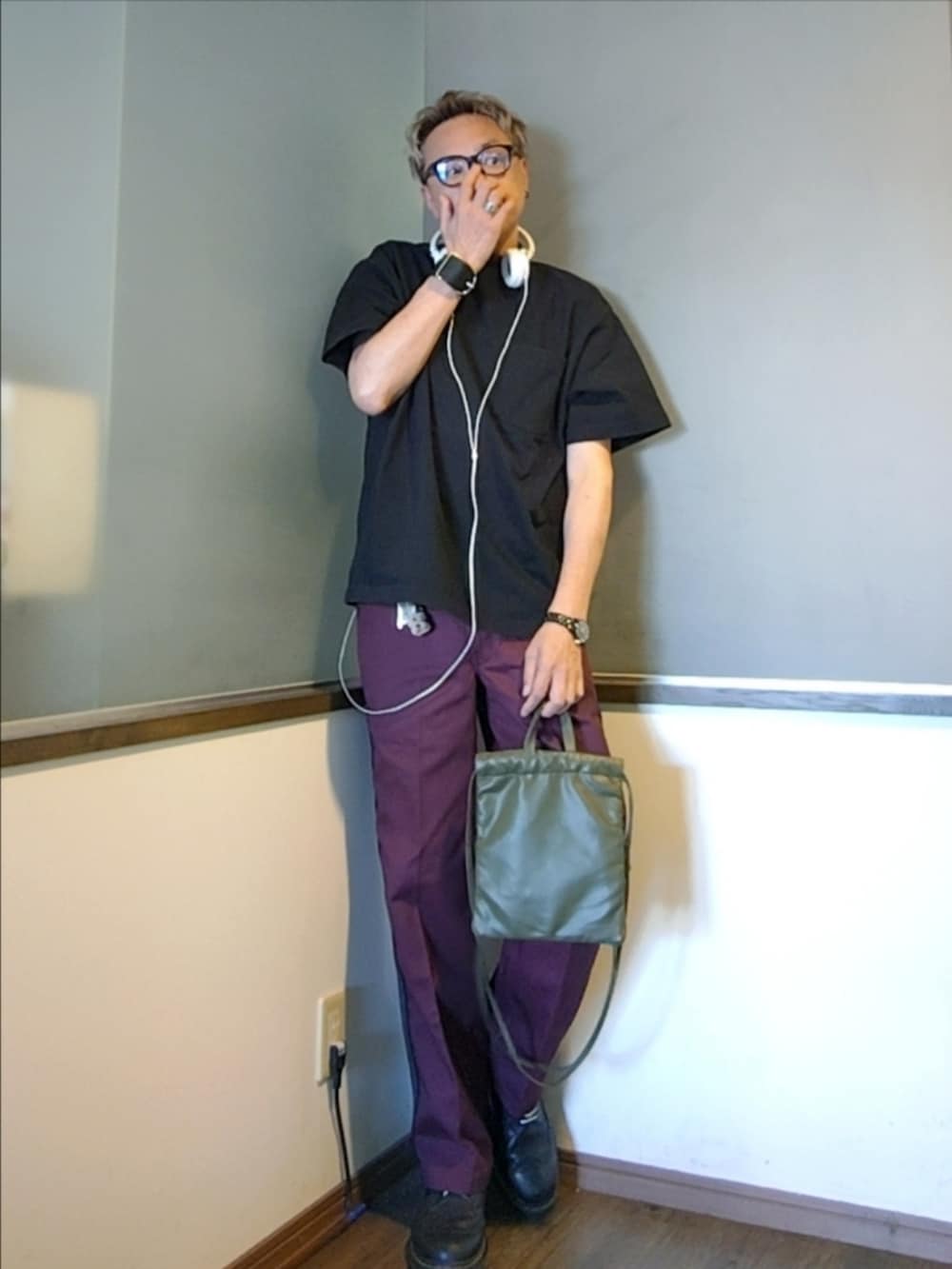 レッド系のチノパンツ、グリーン系のショルダーバッグ、ブラック系のTシャツ/カットソーを着用したメンズの秋コーディネートの2枚目の写真