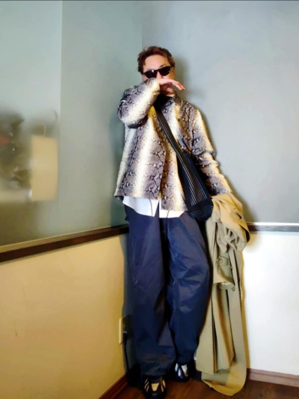 ホワイト系のナイロンジャケット、ベージュ系のトレンチコート、ブラック系のショルダーバッグを着用したメンズの春コーディネートの2枚目の写真