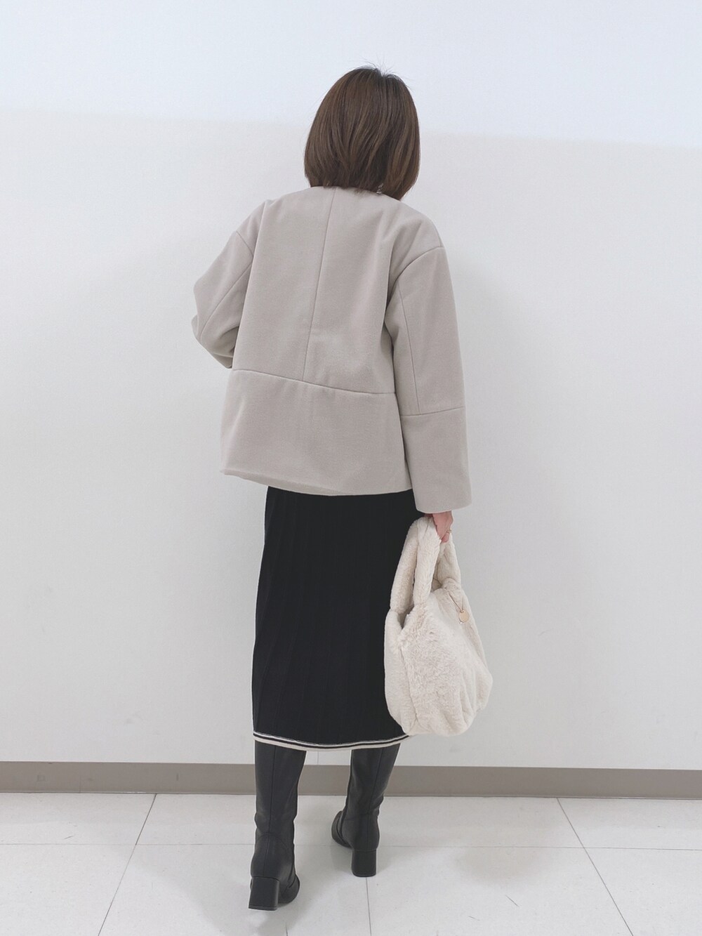 ベージュ系のノーカラーコート、ブラック系のワンピース、ブラック系のブーツを着用したレディースの冬コーディネートの3枚目の写真