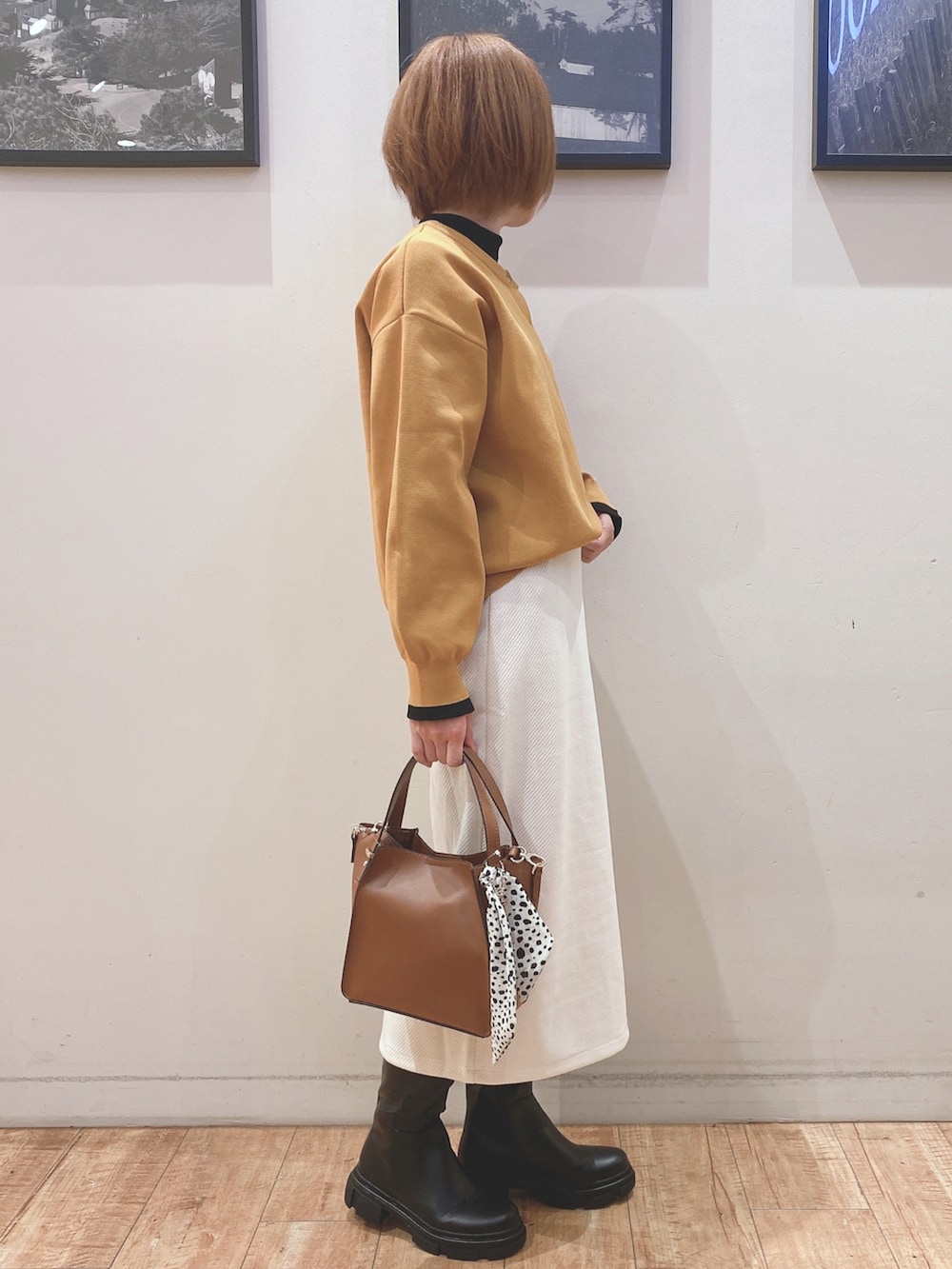 ブラック系のブーツ、イエロー系のカーディガン/ボレロ、ホワイト系のスカートを着用したレディースの秋コーディネートの2枚目の写真