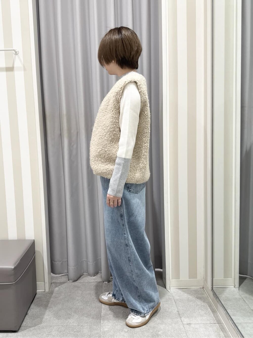 ベージュ系のベスト、グレー系のニット/セーター、ブルー系のデニムパンツを着用したレディースの秋コーディネートの2枚目の写真