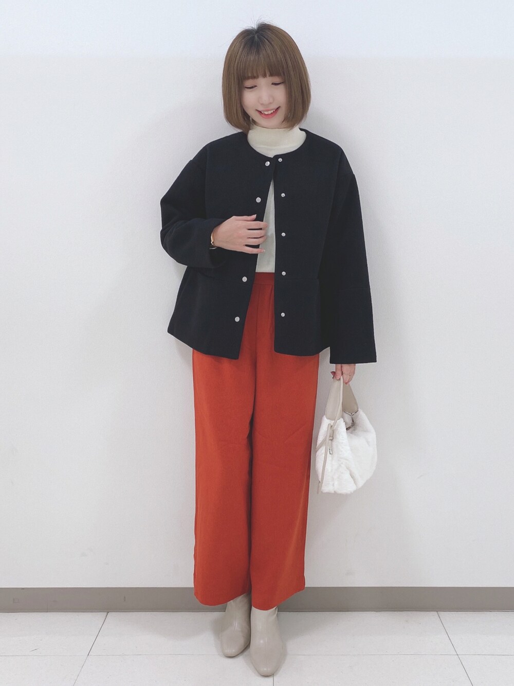 ブラック系のノーカラーコート、ホワイト系のニット/セーター、オレンジ系のその他パンツを着用したレディースの秋コーディネートの4枚目の写真