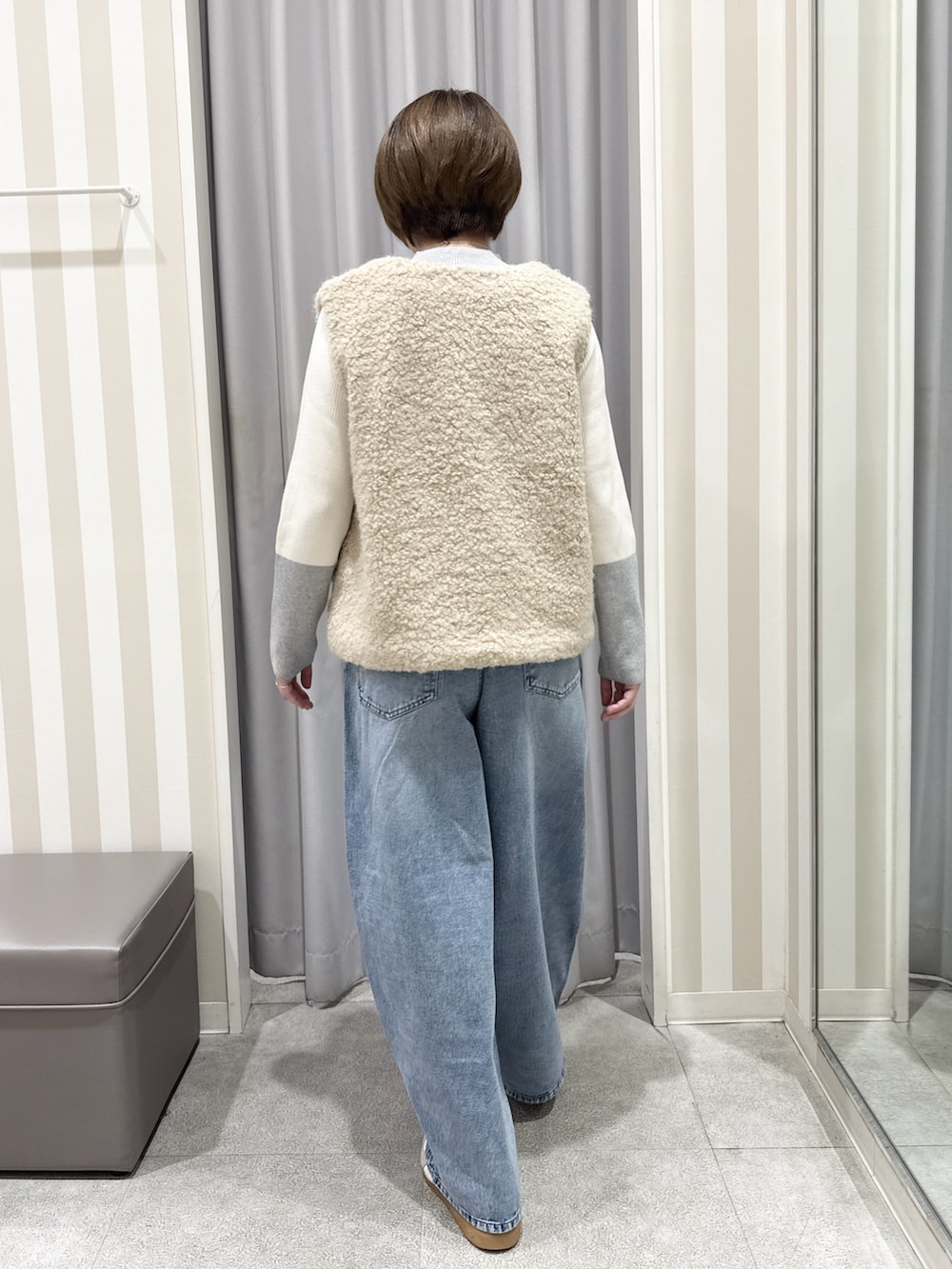 ベージュ系のベスト、グレー系のニット/セーター、ブルー系のデニムパンツを着用したレディースの秋コーディネートの3枚目の写真