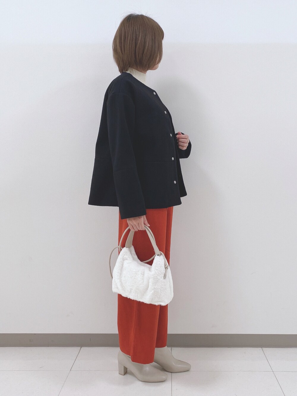 ブラック系のノーカラーコート、ホワイト系のニット/セーター、オレンジ系のその他パンツを着用したレディースの秋コーディネートの2枚目の写真