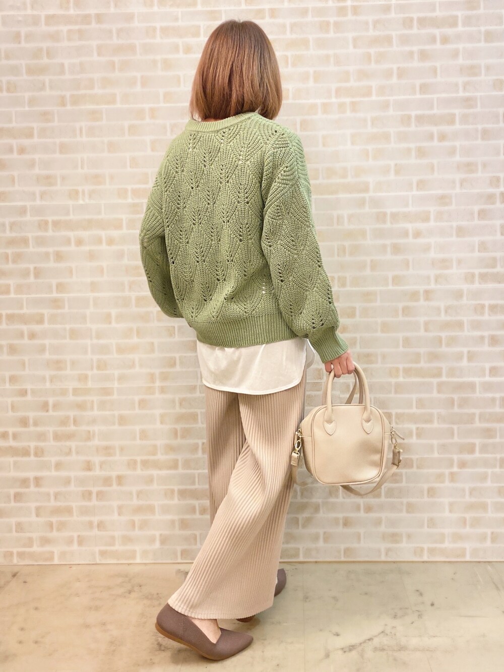 グリーン系のニット/セーター、ブラウン系のパンプス、ホワイト系のショルダーバッグを着用したレディースの冬コーディネートの2枚目の写真