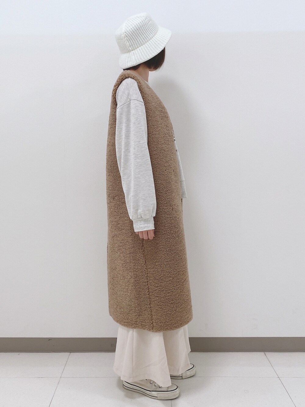 イエロー系のベスト、グレー系のスウェット、ホワイト系のスカートを着用したレディースの秋コーディネートの2枚目の写真