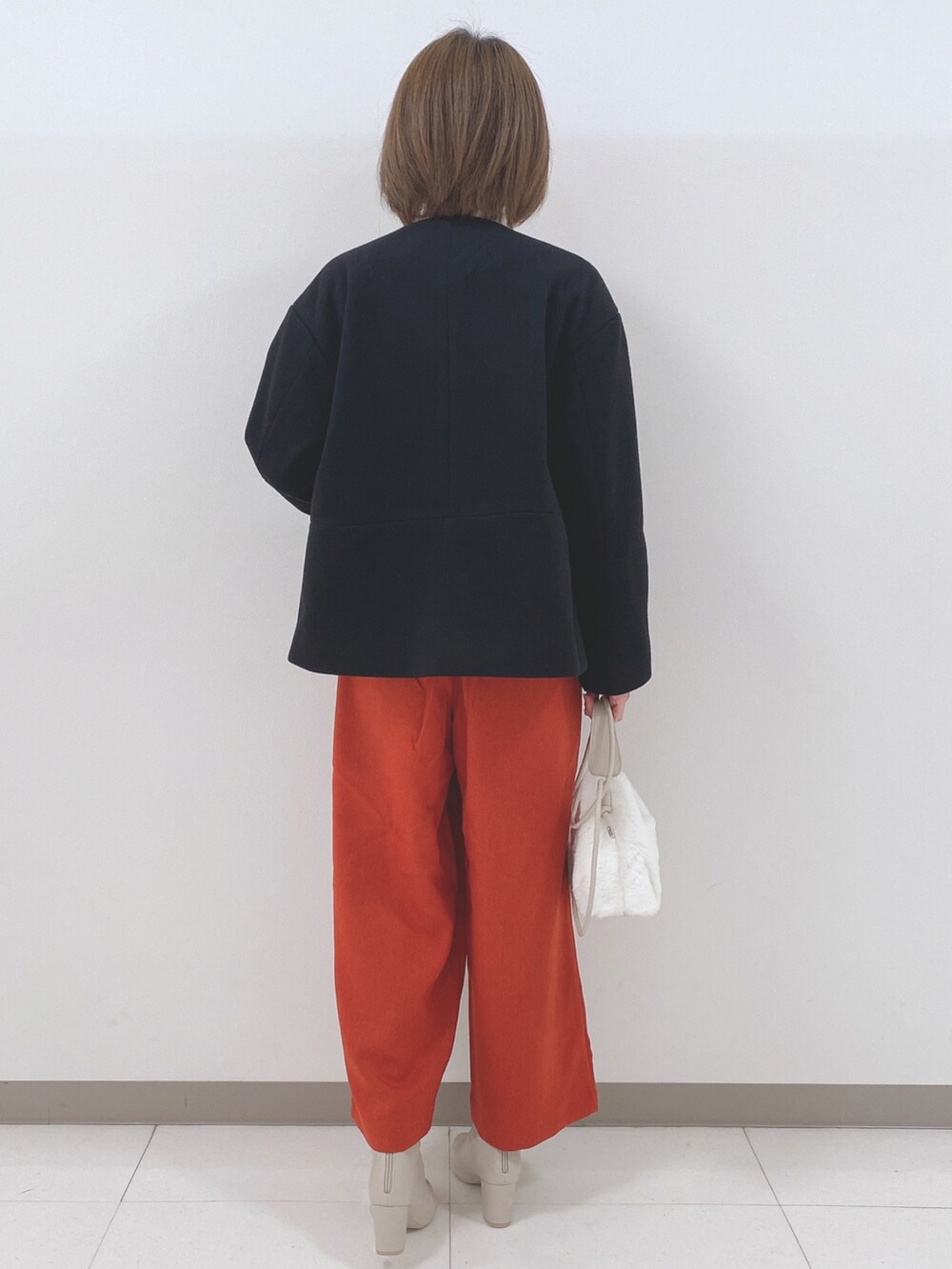 ブラック系のノーカラーコート、ホワイト系のニット/セーター、オレンジ系のその他パンツを着用したレディースの秋コーディネートの3枚目の写真