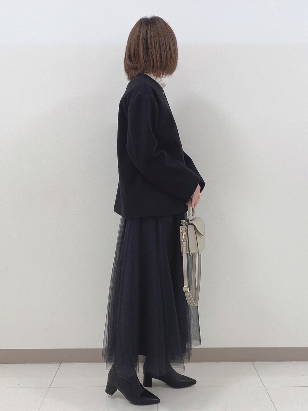 ブラック系のノーカラーコート、ホワイト系のシャツ/ブラウス、ブラック系のスカートを着用したレディースの冬コーディネートの2枚目の写真