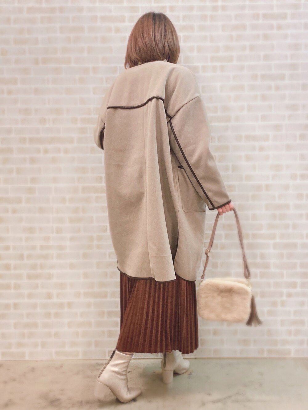 ベージュ系のノーカラーコート、ベージュ系のニット/セーター、ホワイト系のTシャツ/カットソーを着用したレディースの冬コーディネートの2枚目の写真