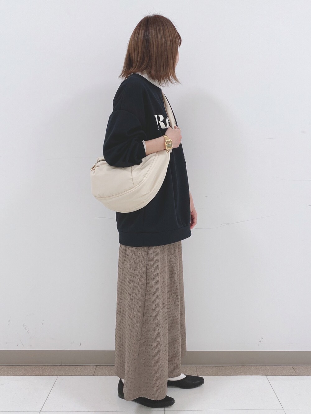 ブラック系のスウェット、ベージュ系のスカート、ブラック系のパンプスを着用したレディースの春コーディネートの2枚目の写真