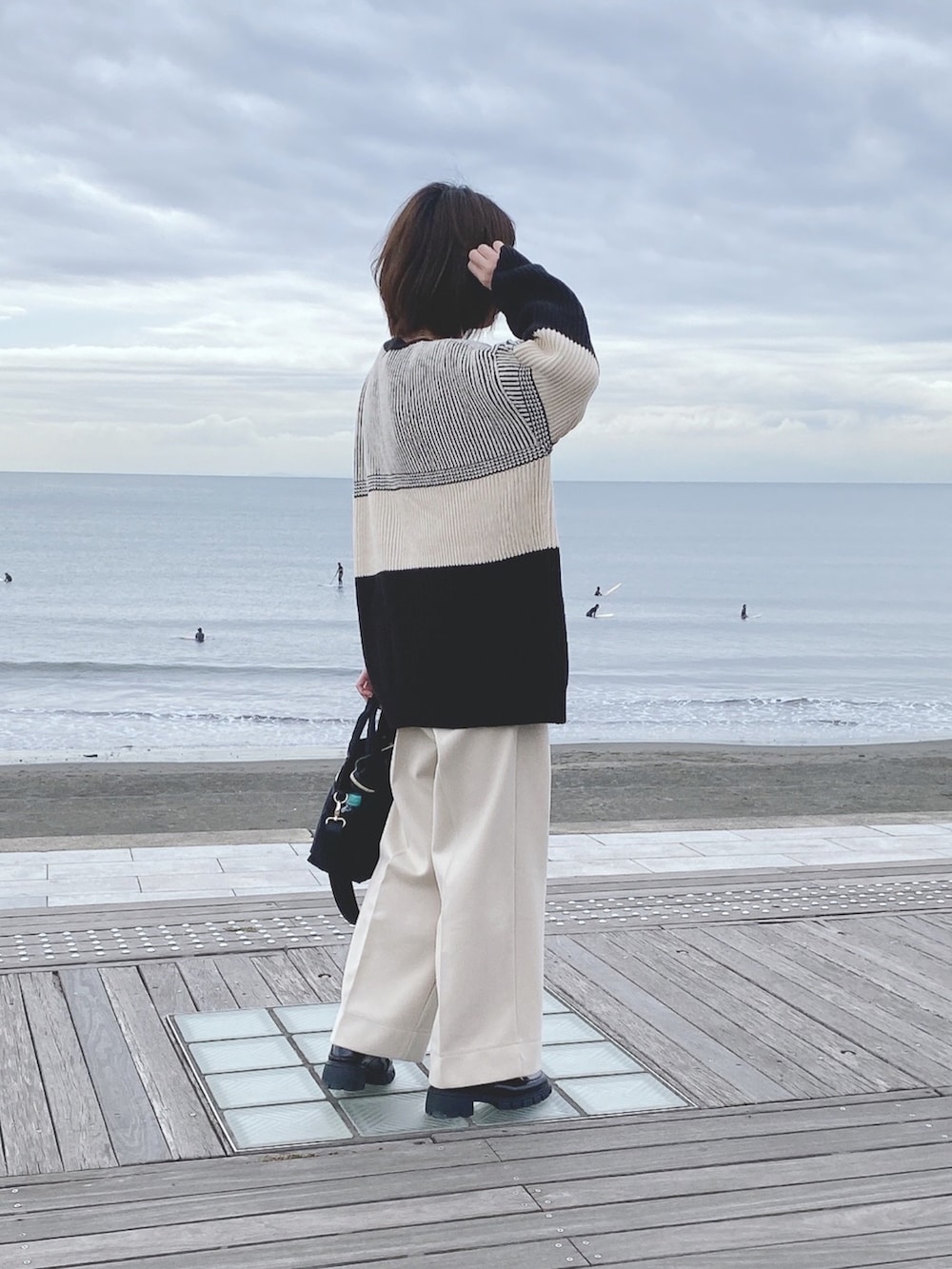 ブラック系のニット/セーター、ホワイト系のパンツ、ブラック系のトートバッグを着用したレディースの冬コーディネートの2枚目の写真