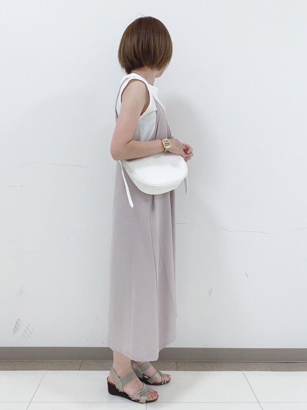 ベージュ系のワンピース、ゴールド系のサンダル、ホワイト系のショルダーバッグを着用したレディースの夏コーディネートの2枚目の写真