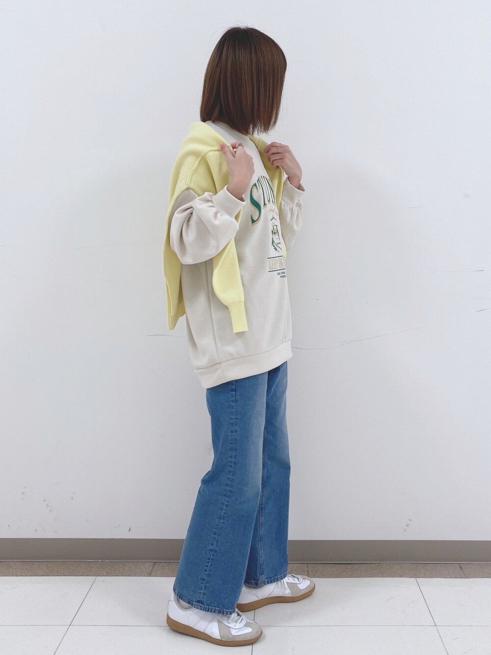 ベージュ系のスウェット、イエロー系のニット/セーター、ブルー系のデニムパンツを着用したレディースの冬コーディネートの2枚目の写真