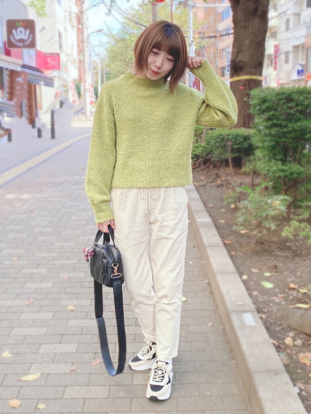 グリーン系のニット/セーター、ブラック系のショルダーバッグ、ベージュ系のスニーカーを着用したレディースの秋コーディネートの2枚目の写真