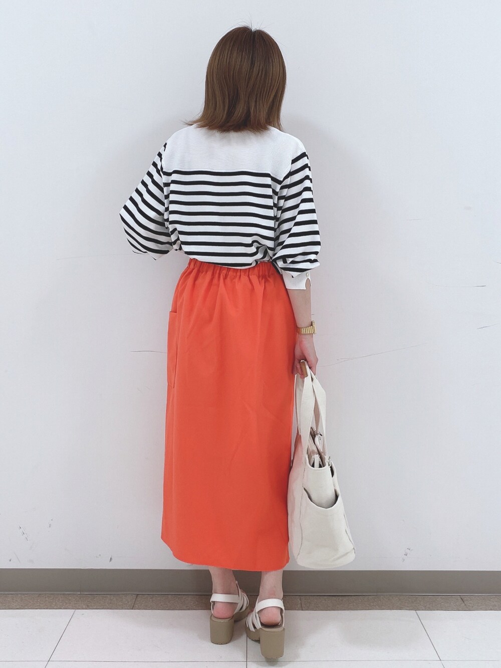 ブラック系のニット/セーター、オレンジ系のスカート、ホワイト系のサンダルを着用したレディースの春コーディネートの3枚目の写真