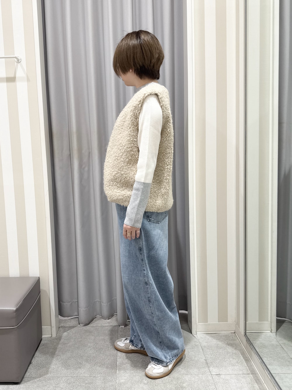 ベージュ系のベスト、グレー系のニット/セーター、ブルー系のデニムパンツを着用したレディースの秋コーディネートの2枚目の写真