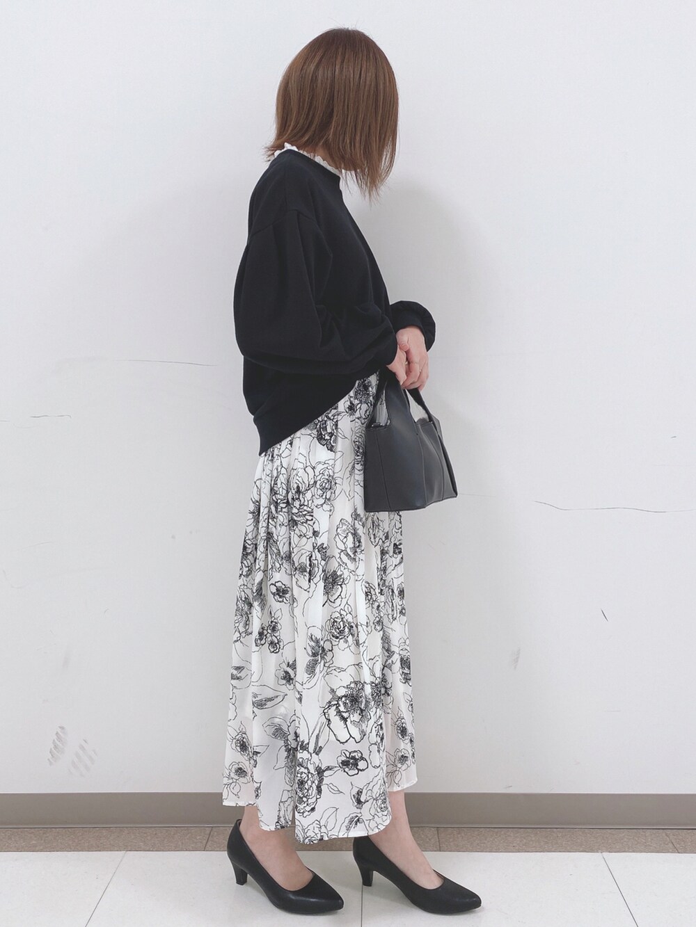 ブラック系のスウェット、ホワイト系のスカート、ブラック系のパンプスを着用したレディースの春コーディネートの2枚目の写真