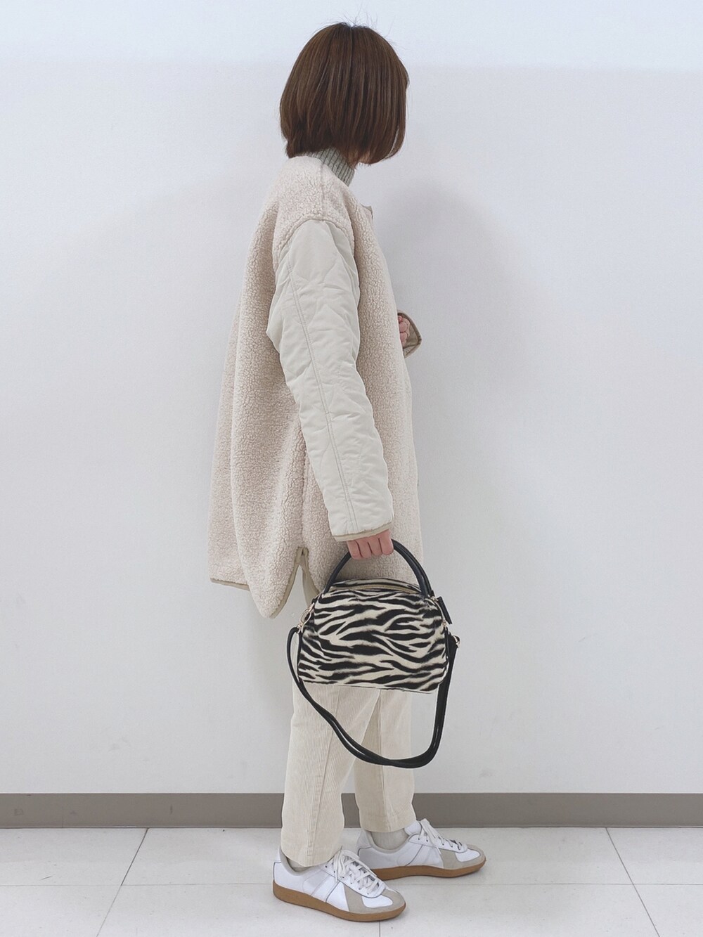 ベージュ系のノーカラージャケット、ベージュ系のニット/セーター、ホワイト系のスニーカーを着用したレディースの秋コーディネートの2枚目の写真